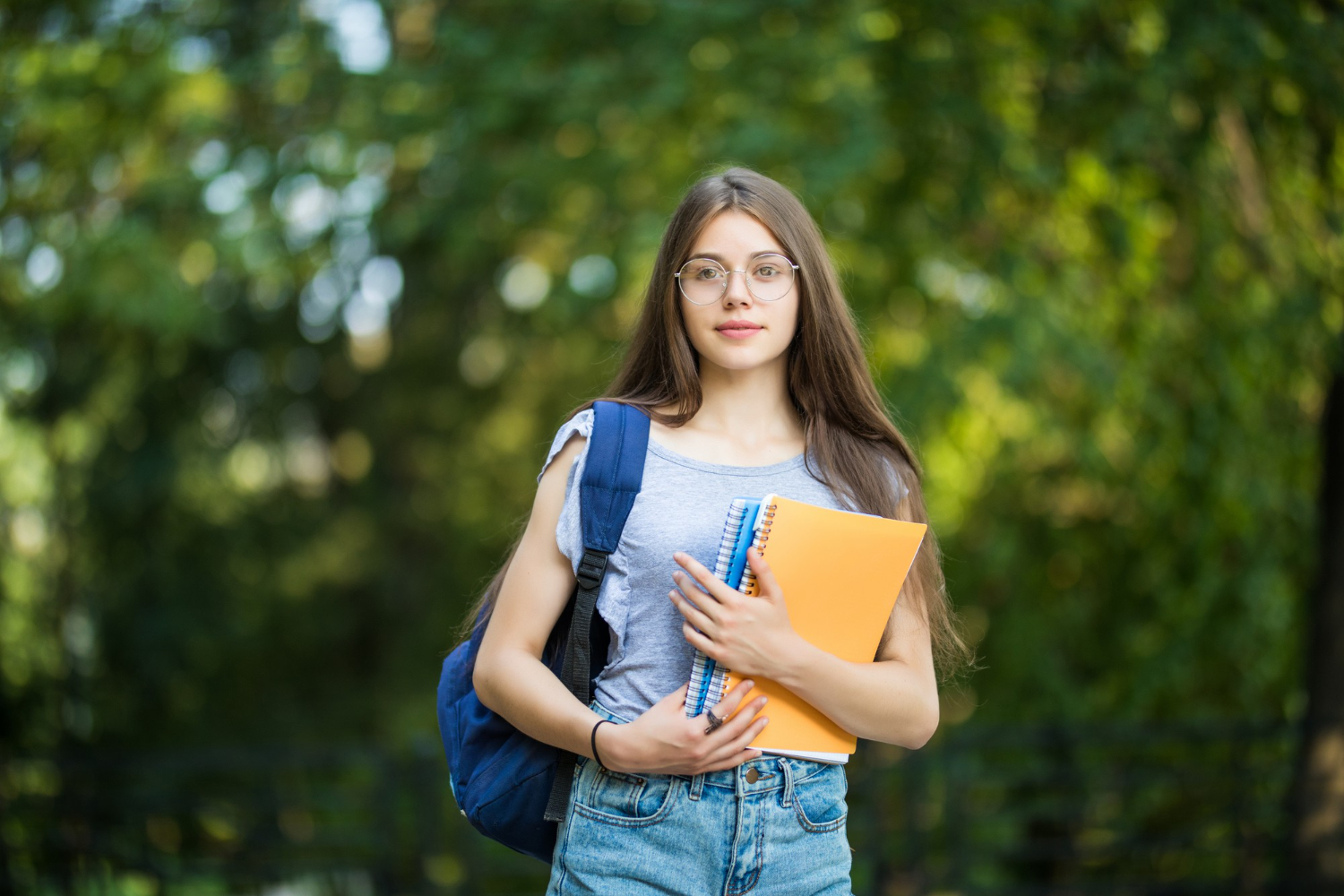 cheerful-attractive-young-woman-with-backpack-notebooks-standing-smiling-park